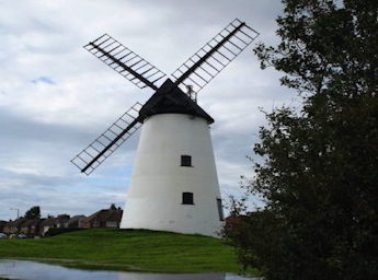 White windmill with grass at the front.