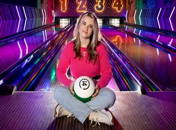 A picture of a woman holding a bowling ball in front of bowling lanes.