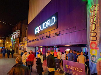 A picture of the Popworld main entrance at night with people queueing.