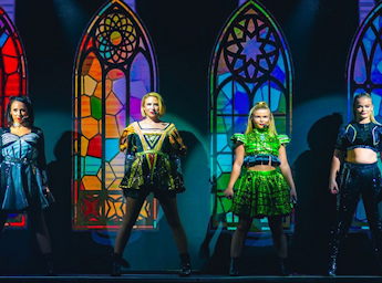 A picture of 4 women singers in colourful outfits with pictures of church windows in the background.